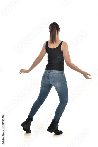full length portrait of brunette girl wearing black single and jeans. standing pose with back to the camera. isolated on white studio background.