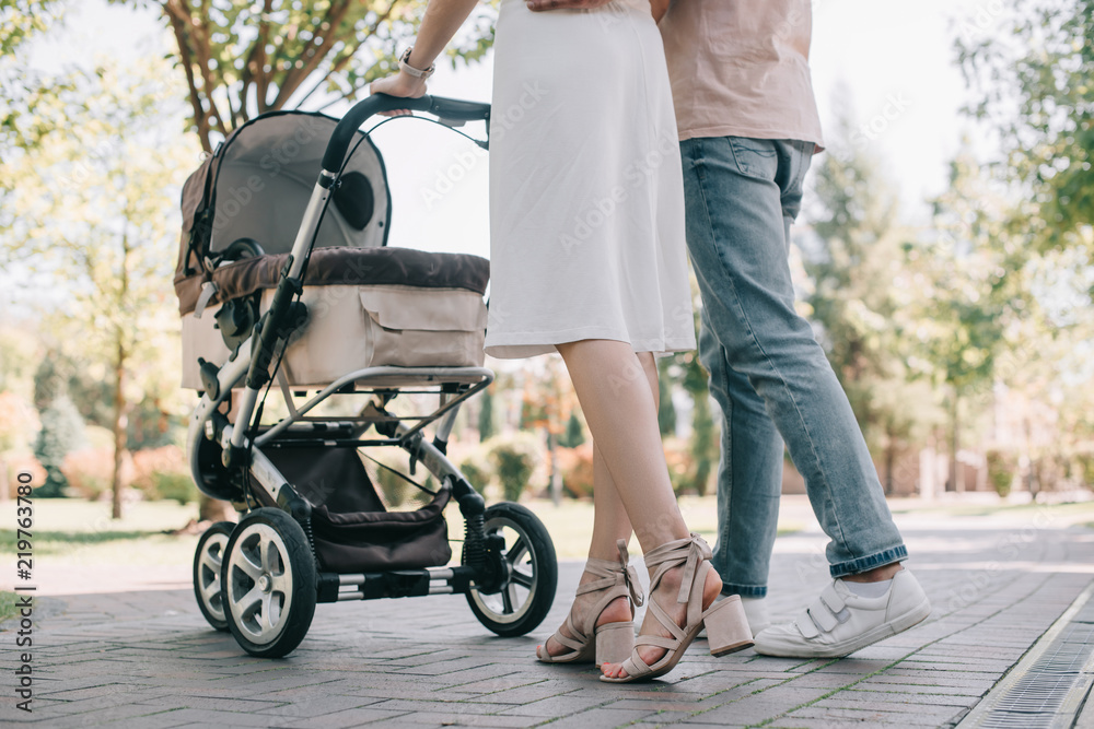 Obraz premium cropped image of parents walking with baby carriage in park