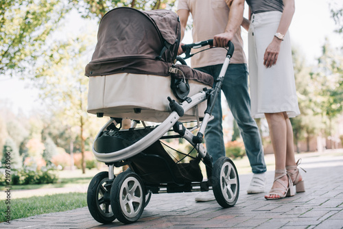 cropped image of mother and father walking with baby carriage in park