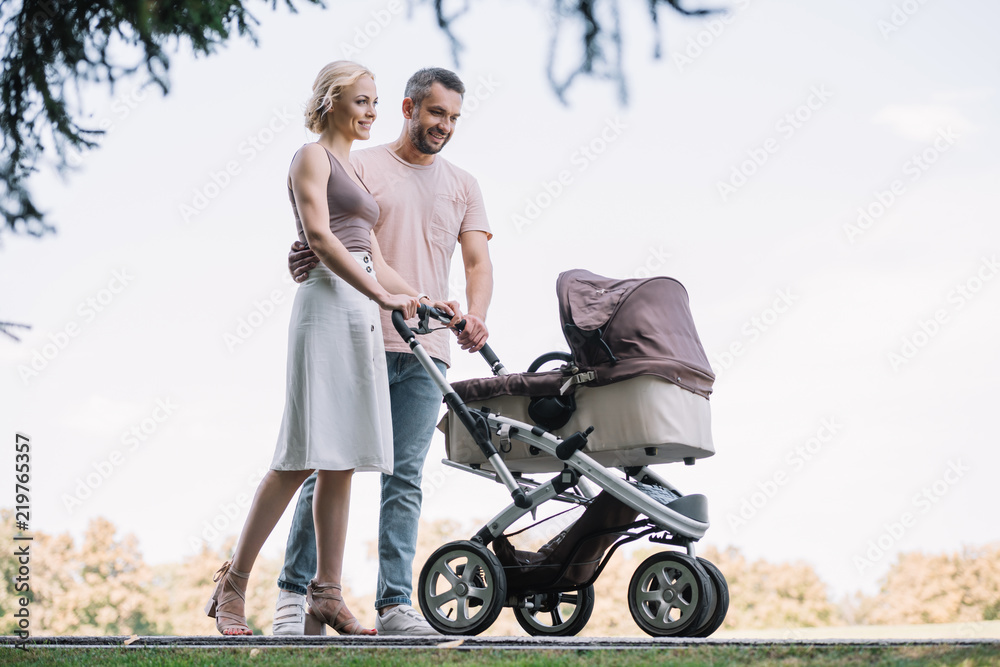 happy parents walking with baby carriage in park at weekend happy parents walking with baby carriage in park at weekend