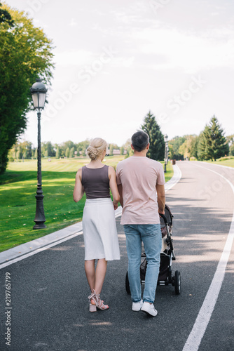 rear view of parents walking with baby carriage on road in park