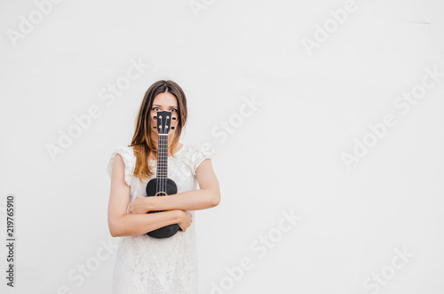 Stylish, beautiful girl with a ukulele in her hands, stands on the background and looks at the camera.