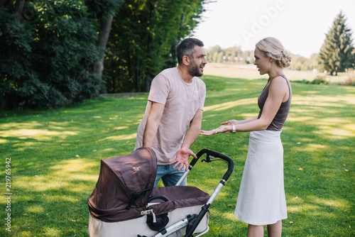 side view of parents quarreling near baby carriage in park