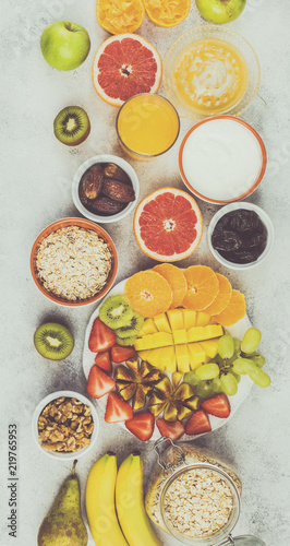 Top view of healthy breakfast with oats, variety of fruits, strawberries, mango, grapes, served on the white table, selective focus. Toned photo
