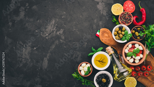 Cooking a caprese salad. Mozzarella cheese, cherry tomatoes, olives, basil leaves, oil, pepper. On a black stone table. Free space for text.