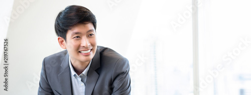 Young smiling Asian businessman in white office banner background