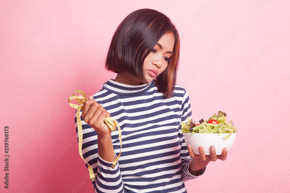 Unhappy Asian woman with measuring tape and salad. Unhappy Asian woman with measuring tape and salad.