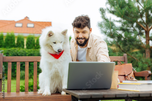 Smiling man. Bearded handsome man smiling broadly while showing photos on laptop his white dog