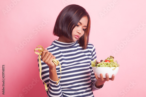 Unhappy Asian woman with measuring tape and salad.