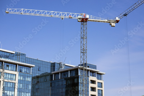 Construction of the building with a tower crane. Construction site, tower crane, building with glass finish, blue sky background.