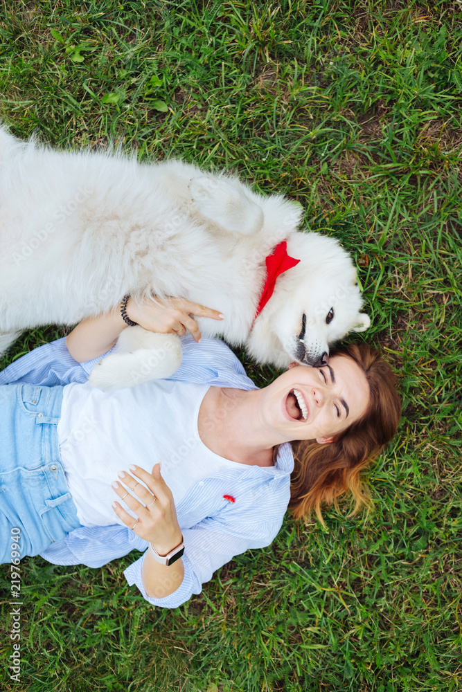 Petting dog. Appealing blonde-haired woman smiling broadly while petting her white fluffy dog Petting dog. Appealing blonde-haired woman smiling broadly while petting her white fluffy dog
