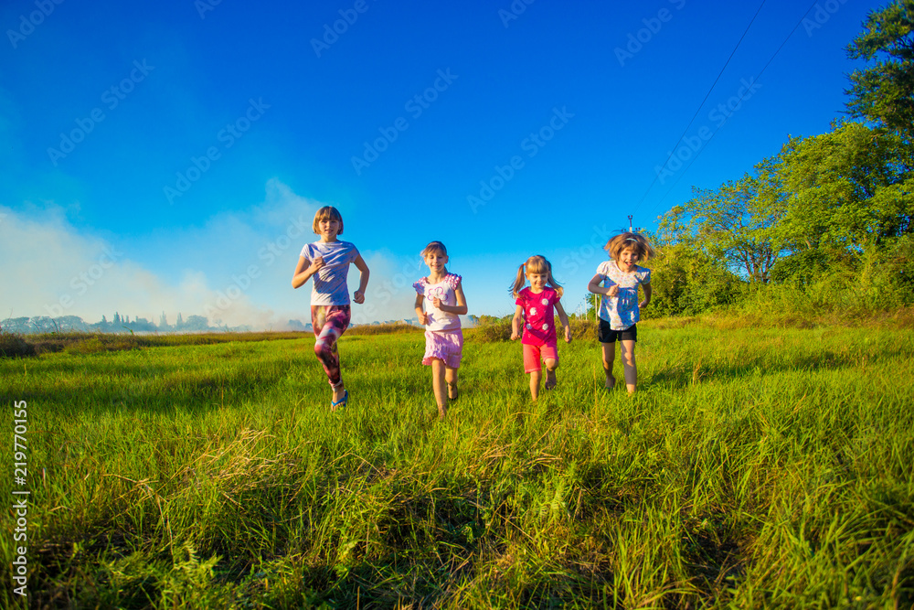 Group of happy kids running in green summer field