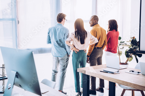 back view of multiethnic business colleagues looking out window in office