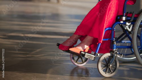 Girl in a wheelchair, in the frame of female legs in red shoes photo