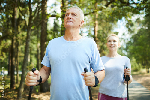 Active aged man and woman in sportswear enjoying summer day in natural environment while trekking