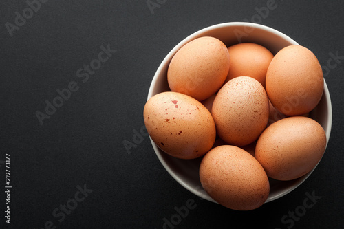 brown eggs in bowl isolated on dark background. top view