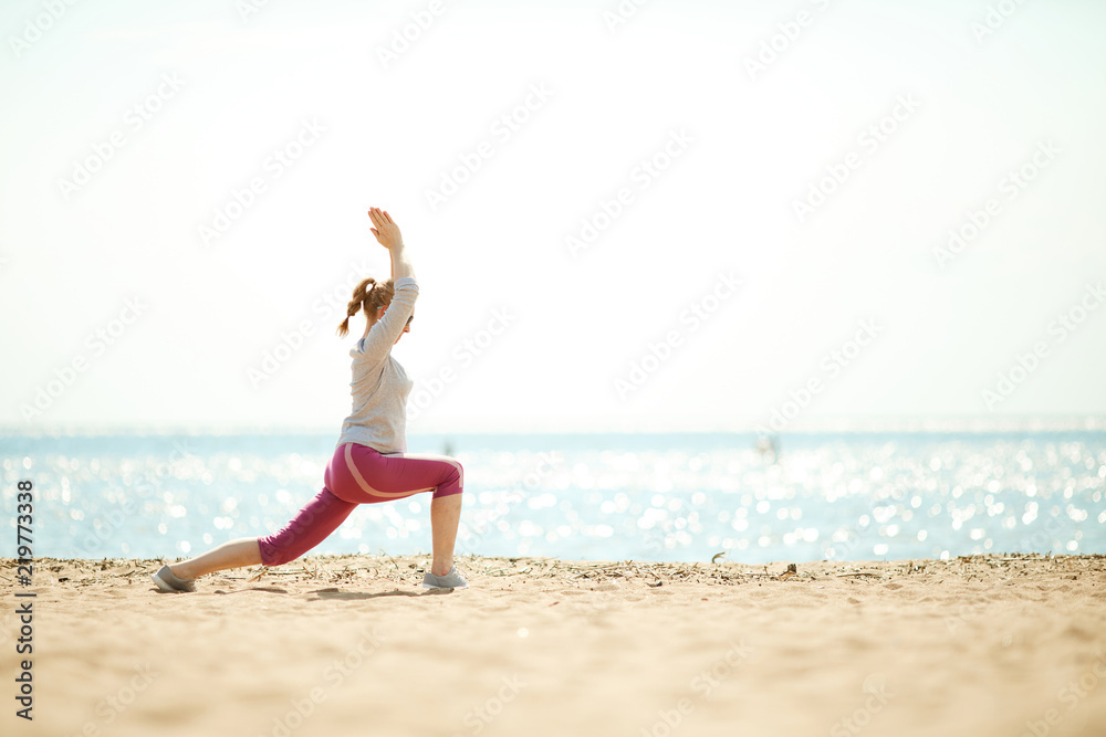 Side view of active female doing exercises for leg stretch and arms by waterside