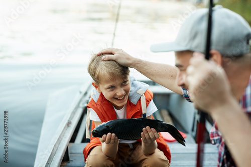 Happy boy holding big fish, and showing it to his father, while they are on the boat