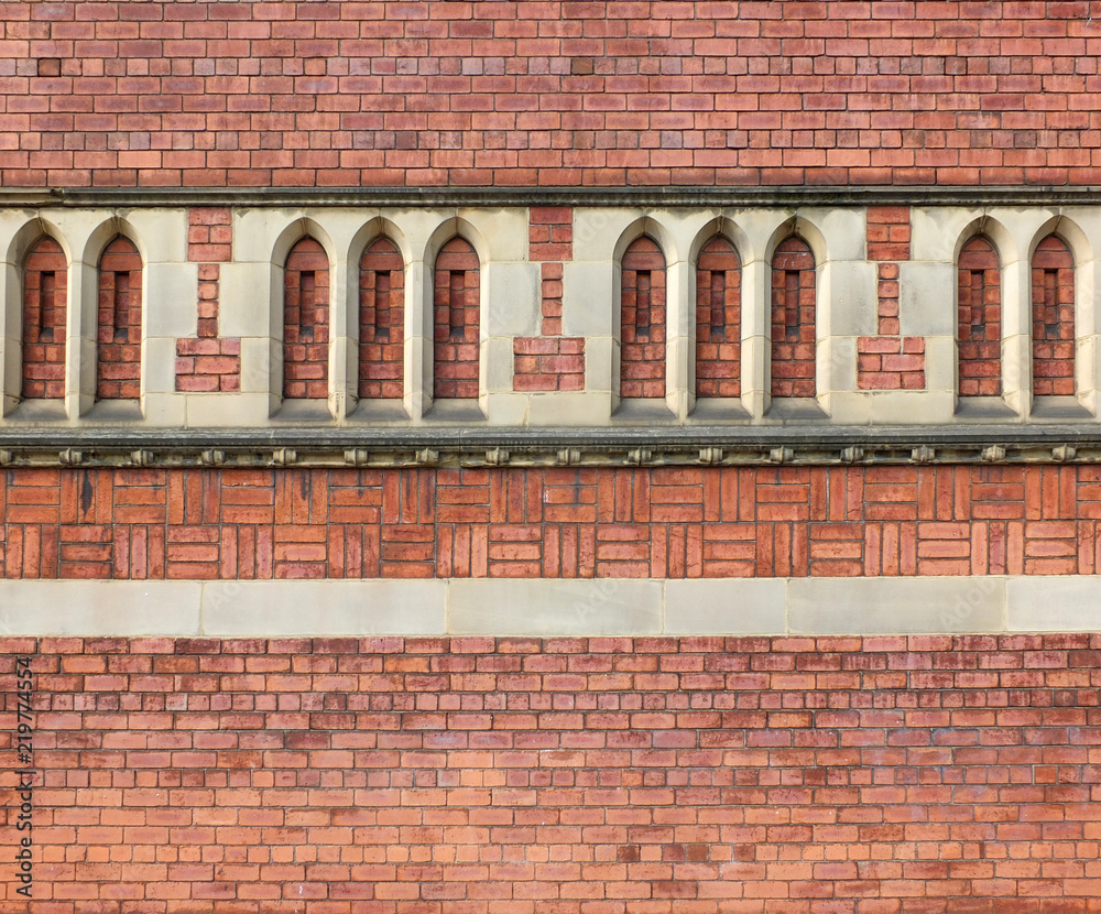 ornate red brick wall built with complex patterns and gothic style stone decorative arch detailing on a large old building