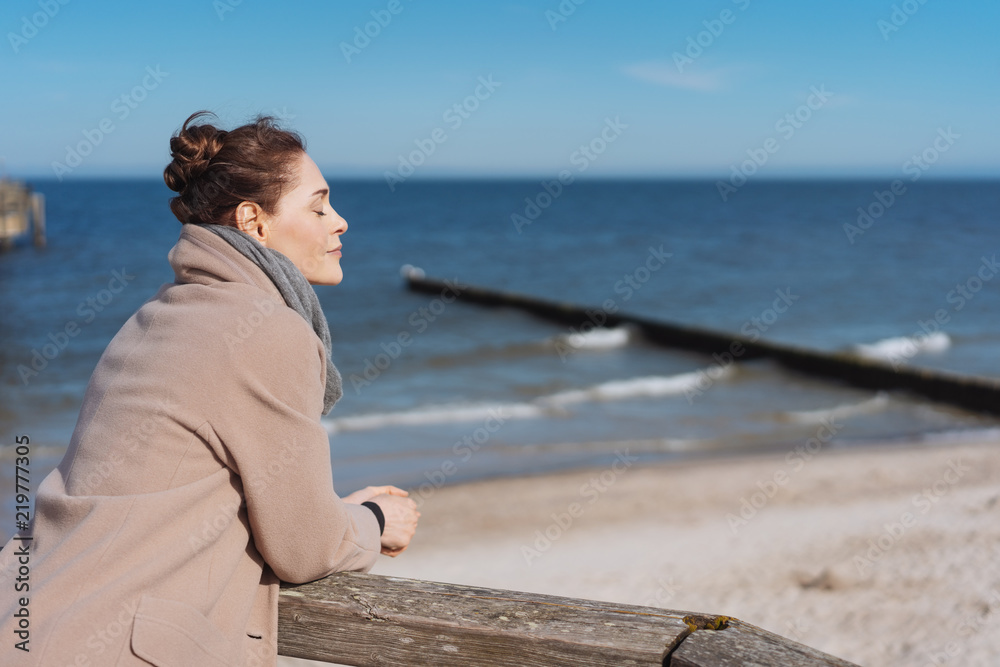 frau steht im winter am meer und genießt die sonne frau steht im winter am meer und genießt die sonne
