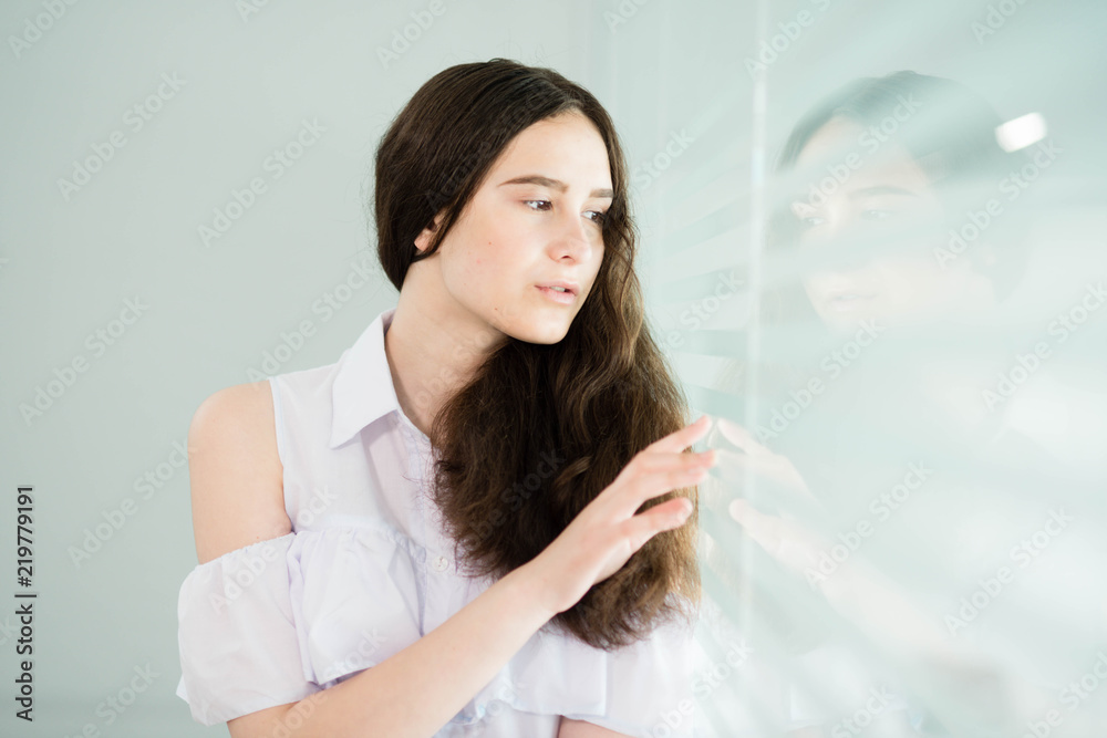 a girl in a white shirt and with her hair down is standing near the window a girl in a white shirt and with her hair down is standing near the window
