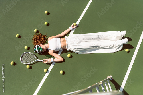 overhead view of stylish woman in white clothing and cap lying with racket lying on tennis court with racket © LIGHTFIELD STUDIOS