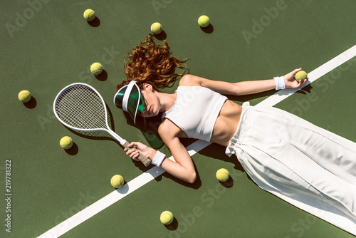 overhead view of stylish woman in white clothing and cap lying with racket lying on tennis court with racket © LIGHTFIELD STUDIOS
