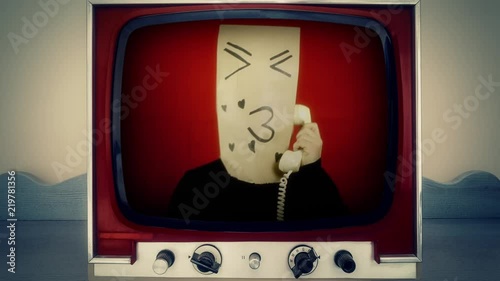 A retro vintage TV showing a weird loving kissing breadbag face, in a conversation on a rotary telephone. Close-up shot.
 photo