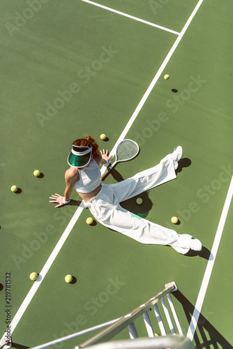 high angle view of beautiful woman in stylish white clothing sitting on tennis court with balls and racket around © LIGHTFIELD STUDIOS