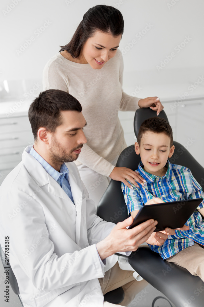 medicine, dentistry and healthcare concept - dentist showing tablet pc computer to kid patient and his mother at dental clinic medicine, dentistry and healthcare concept - dentist showing tablet pc computer to kid patient and his mother at dental clinic