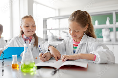 education, science and children concept - kids studying chemistry at school laboratory and writing to workbooks