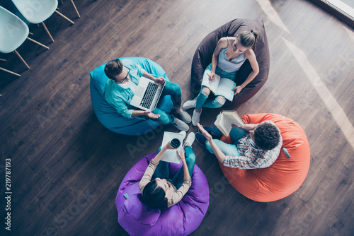 High top angle view of diversity stylish and modern hipster youngster sit in colorful armchairs on the wooden floor work together on the task sit classmates chair bag