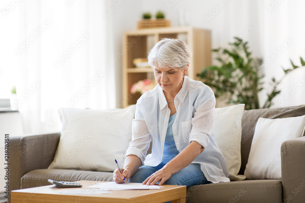 business, savings, annuity insurance, age and people concept - senior woman with papers or bills and calculator writing at home business, savings, annuity insurance, age and people concept - senior woman with papers or bills and calculator writing at home