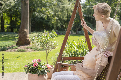 Smiling caregiver and happy elderly woman on the terrace during sunny day photo