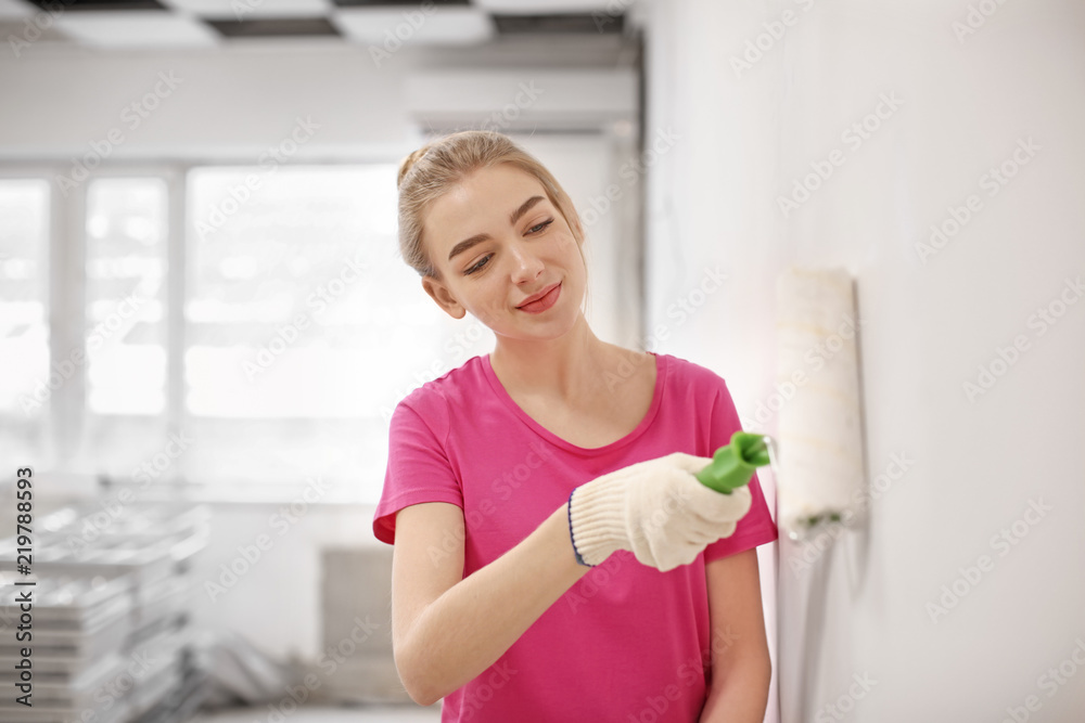 Female decorator painting wall with roller indoors Female decorator painting wall with roller indoors