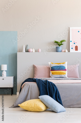 Blue blanket on bed with colorful pillows in modern bedroom interior with plant. Real photo