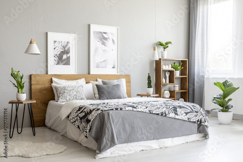 Patterned blanket on wooden bed in grey bedroom interior with plants and posters. Real photo photo