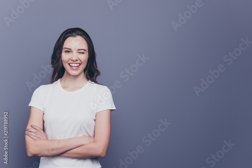 Adorable attractive nice charming gorgeous curly-haired brunette caucasian smiling winking young girl with folded hands. Copy space. Isolated over grey background