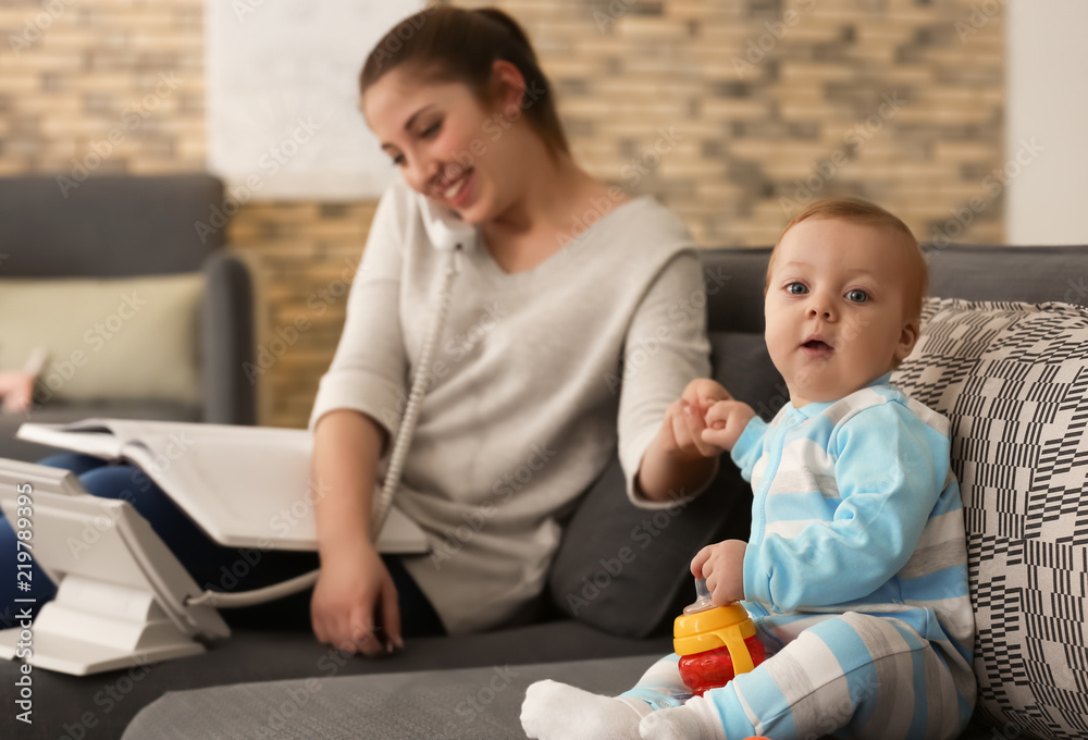 Cute little baby sitting on sofa while mother working at home Cute little baby sitting on sofa while mother working at home