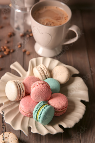 Plate with tasty macarons and coffee set on table
