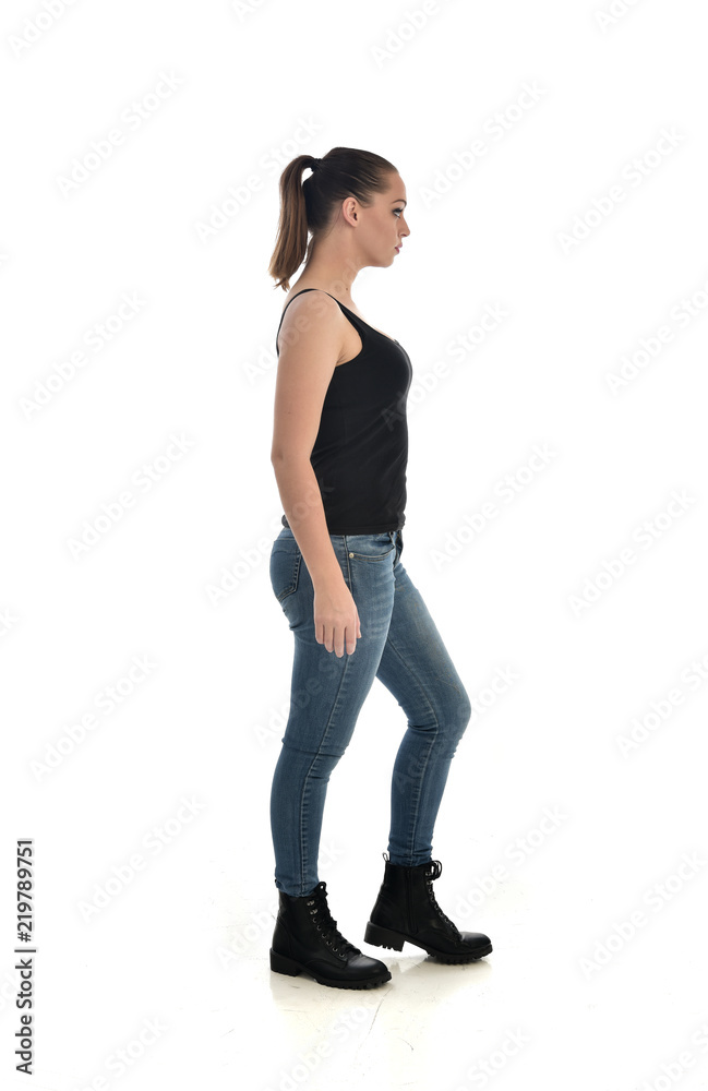 full length portrait of brunette girl wearing black single and jeans. standing pose in side profile. isolated on white studio background. full length portrait of brunette girl wearing black single and jeans. standing pose in side profile. isolated on white studio background.