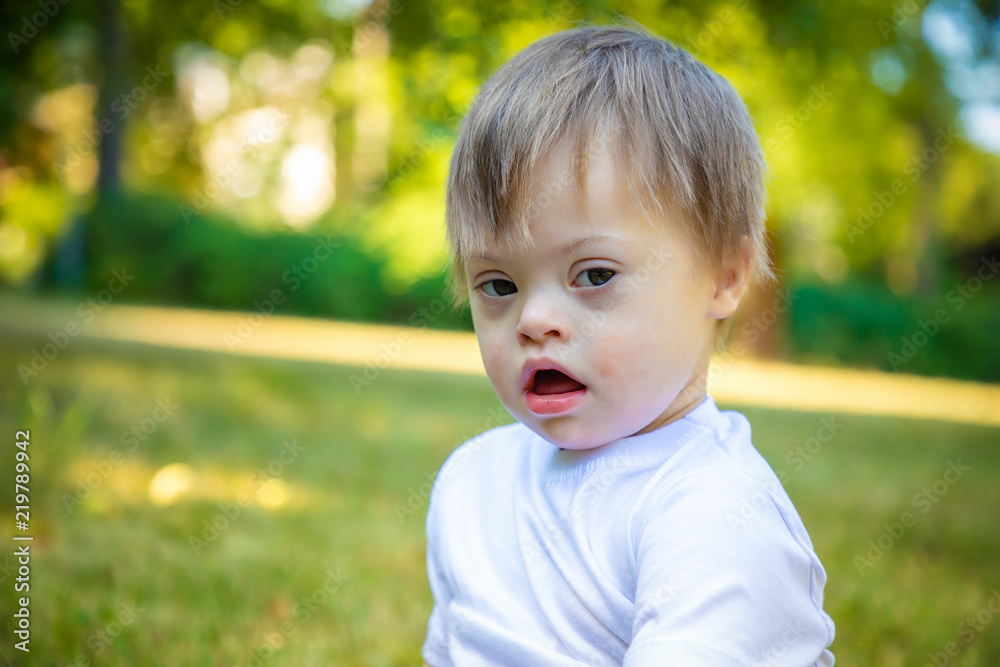 Portrait of Cute small boy with Down syndrome playing in summer day on nature Portrait of Cute small boy with Down syndrome playing in summer day on nature
