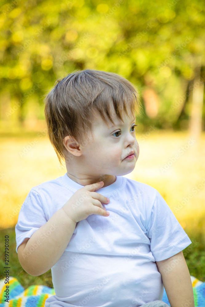 Portrait of Cute small boy with Down syndrome playing on blanket in summer day on nature Portrait of Cute small boy with Down syndrome playing on blanket in summer day on nature