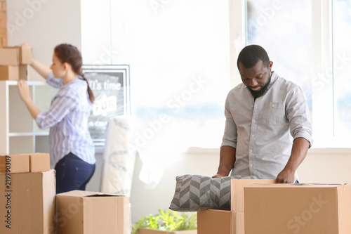 Interracial couple unpacking boxes indoors. Moving into new house © Pixel-Shot