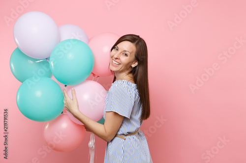Portrait of pretty laughing young happy woman wearing blue dress holding colorful air balloons isolated on bright trending pink background. Birthday holiday party, people sincere emotions concept.
