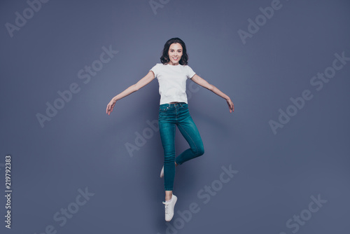 Graceful attractive adorable pretty stylish trendy nice lovely cheerful curly-haired brunette girl in casual white t-shirt and jeans  raising up in air  isolated on grey background