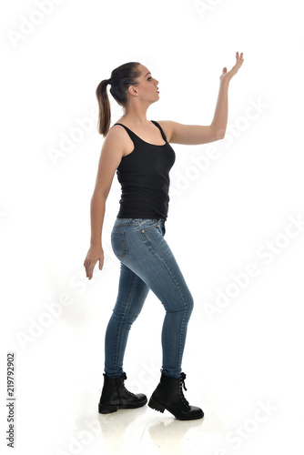  full length portrait of brunette girl wearing black single and jeans. standing pose in side profile. isolated on white studio background.