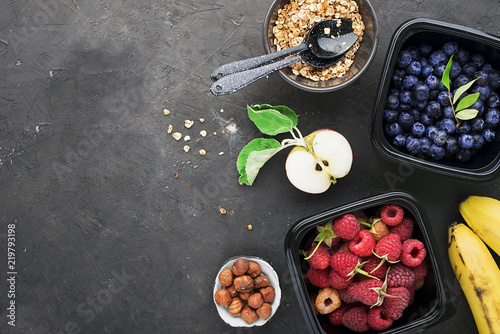 Black plastic containers take-away for a healthy snack food with raspberries, blueberries. Ingredients of healthy breakfast: granola, oat flakes, berries, nuts, apples, bananas. Top View.