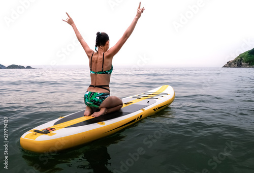 Vacations at sea: the girl sails on a yellow sup-board and on sea waves and happily lifts her hands to the top.