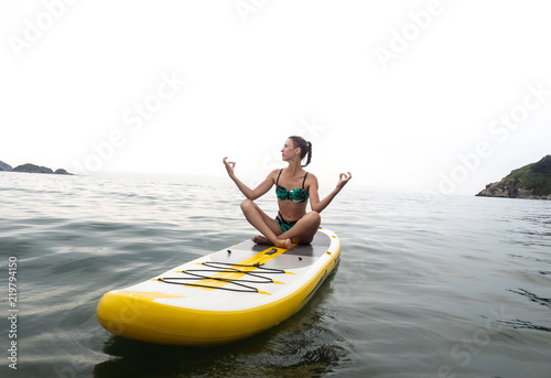 Vacation at sea: the girl sails on a yellow sup-board and meditates in a lotus position. © Aboltin